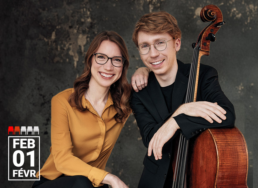 The image shows two individuals smiling warmly. ​Pianist Meagan Milatz is on the left ​and has medium-length brown hair, glasses, and is wearing a mustard-yellow blouse. ​C​ellist Cameron Crozman is on the right ​and has light brown or auburn hair, glasses, and is wearing a black suit jacket while holding a cello. They ​a​re a classical music duo, and the setting has a textured, neutral background.