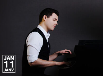 A man in a white dress shirt and black vest is playing a piano. He has short, dark hair and is seated at the piano with a focused expression. The background is dark, and the date "JAN 11" is prominently displayed in the bottom left corner of the image.