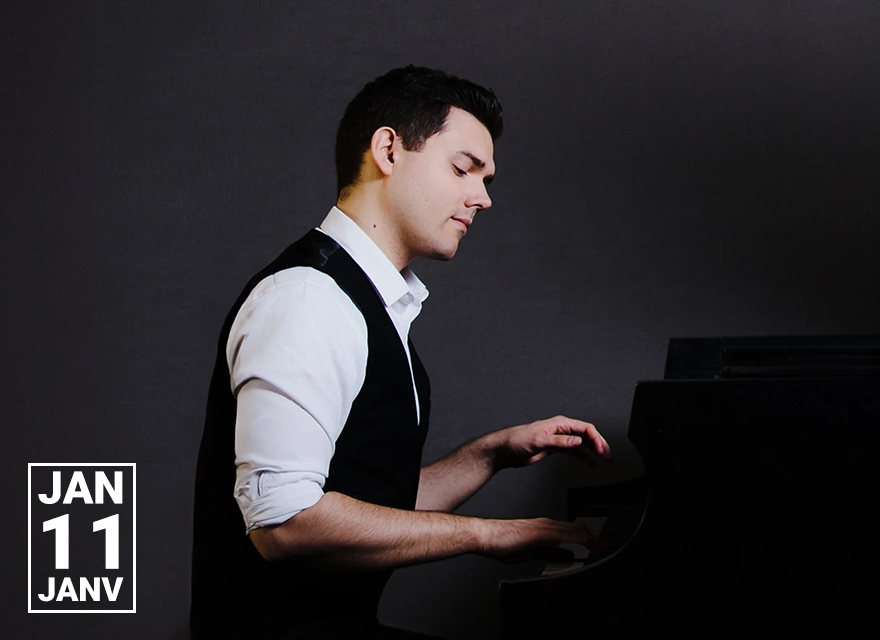 A man in a white dress shirt and black vest is playing a piano. He has short, dark hair and is seated at the piano with a focused expression. The background is dark, and the date "JAN 11" is prominently displayed in the bottom left corner of the image.