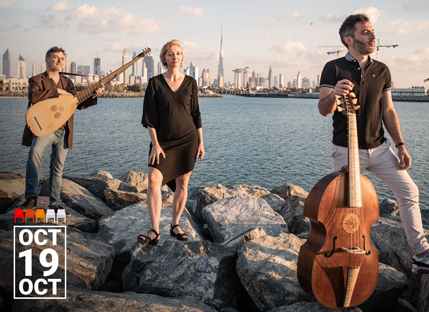 This image shows three members of the French Baroque music ensemble Faenza standing on rocky terrain with a cityscape in the background, including the Burj Khalifa. The date "Oct 19" is prominently displayed in the lower left corner. The person on the left holds a lute, the person in the center stands with their hands at their sides, and the person on the right holds a large stringed instrument called a viola da gamba.