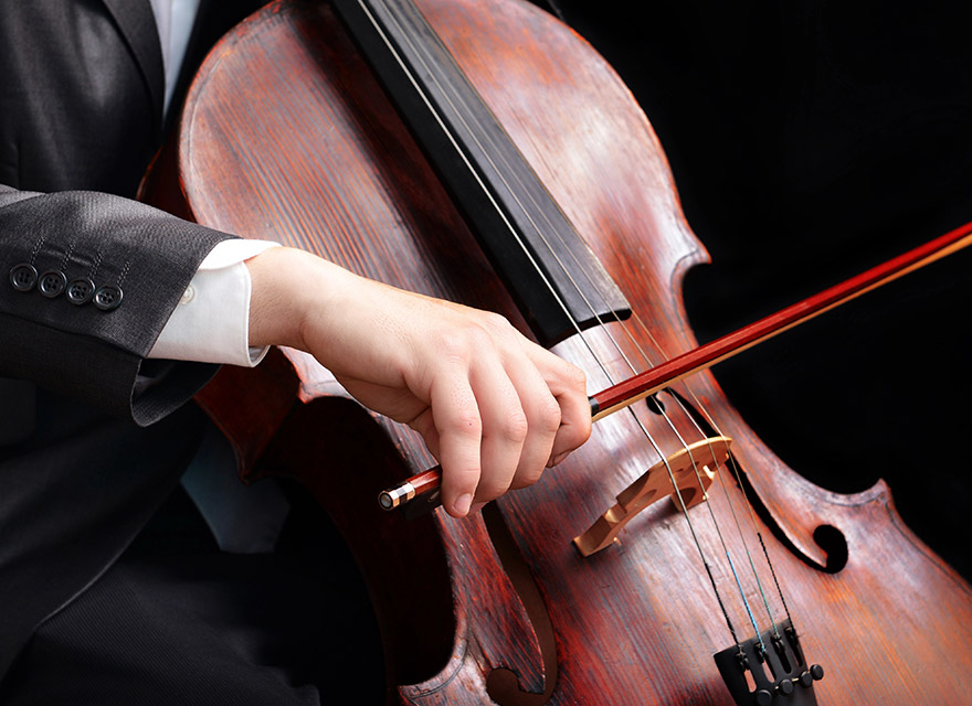 A close-up of a cellist's hand elegantly holding a bow, gliding across the strings of a polished wooden cello, with the musician dressed in formal attire.